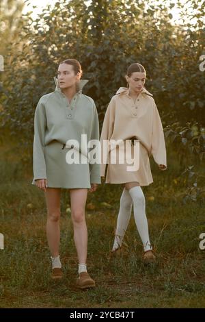 Zwei Models in stylischen Trainingsanzügen posieren bei Sonnenuntergang im Apfelgarten . Das Model trägt einen hellen Trainingsanzug und Rock. Stockfoto