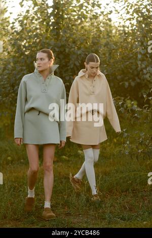 Zwei Models in stylischen Trainingsanzügen posieren bei Sonnenuntergang im Apfelgarten . Das Model trägt einen hellen Trainingsanzug und Rock. Stockfoto