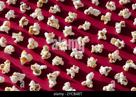 Verstreute Popcorn-Stücke werfen Schatten auf einem leuchtend roten Hintergrund und wecken Nostalgie für Filmabende und Karnevals. Stockfoto