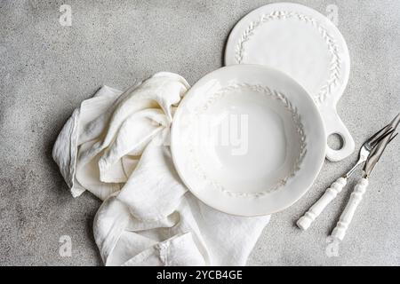 Eine geschmackvolle Präsentation von weiß geprägtem Geschirr, begleitet von einer weichen Leinenserviette und Vintage-Besteck, auf einer dezenten strukturierten Oberfläche, die an das erinnert Stockfoto