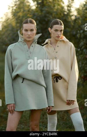 Zwei Models in stylischen Trainingsanzügen posieren bei Sonnenuntergang im Apfelgarten . Das Model trägt einen hellen Trainingsanzug und Rock. Stockfoto