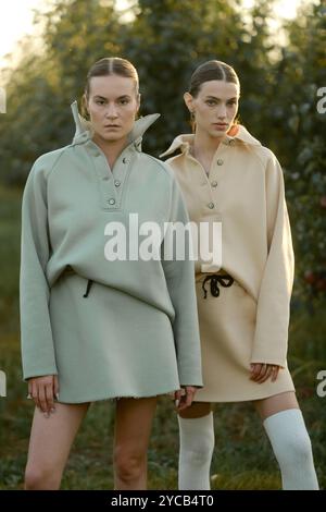 Zwei Models in stylischen Trainingsanzügen posieren bei Sonnenuntergang im Apfelgarten . Das Model trägt einen hellen Trainingsanzug und Rock. Stockfoto