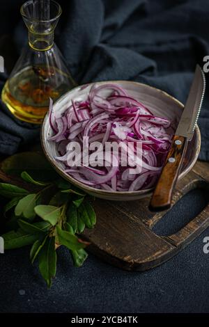 Rote Zwiebeln werden für die Gärung vorbereitet, in einer rustikalen Schüssel mit geschnittenen Zwiebeln, Lorbeerblättern, Pfeffer und Meersalz, Einer Glasflasche spi Stockfoto