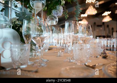 Ein wunderschön gestalteter Hochzeitstisch mit einer Auswahl an Glaswaren, eleganten Dekorationen und dezenten floralen Akzenten unterstreicht die Ambientebeleuchtung Stockfoto