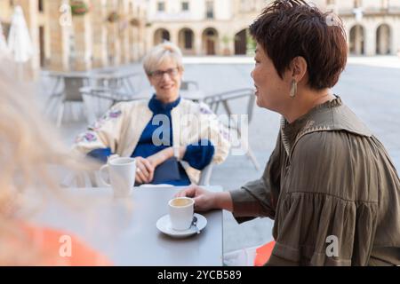 Eine Gruppe reifer Frauen führt lebhafte Gespräche, während sie in einem malerischen Café im Freien Kaffee genießen. Ihre Ausdrücke spiegeln Freude und Freunde wider Stockfoto