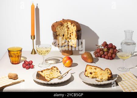 Eine elegante Dining-Präsentation mit einem traditionellen italienischen Panettone auf einem goldenen Stand, gepaart mit zwei Tellern mit geschnittenem Kuchen und umgeben von W Stockfoto