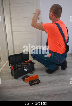 Handwerker steht mit geöffnetem Werkzeugkasten und benutzt einen Schraubendreher, um ein Türschloss zu reparieren. Stockfoto