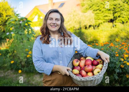 Frische reife Äpfel aus den Obstbäumen, gesammelt von der schönen Bäuerin, die sie mit der Apfelernte vor der Kamera posiert und riecht Stockfoto