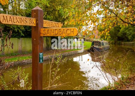 Wegweiser auf dem Trent und Mersey Kanal mit verankertem Schmalboot im Dorf Wheelock Cheshire Stockfoto