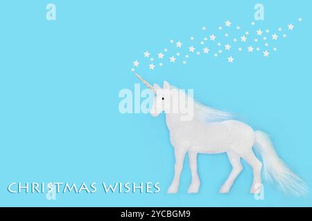 Weihnachtswünsche mit magischer Einhornkugeldekoration auf blauem Hintergrund. Fantasy-Baumschmuck mit weißen Glitzersternen für die Weihnachtszeit. Stockfoto