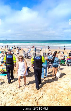 Zwei männliche Soldaten der Polizei von Devon & Cornwall patrouillieren unter Urlaubern, die sich am Fistral Beach in Newquay in Cornwall amüsieren Stockfoto