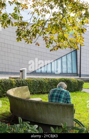 Ein älterer Mann sitzt allein in einem grünen Pace oder auf einer Steinbank außerhalb des Sea City Museums im Stadtzentrum von Southampton, Southampton, Hampshire, Großbritannien Stockfoto