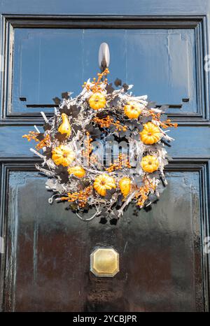 Kranz an einer schwarzen Haustür aus Herbstblumen und Farben, die rund um die Halloween-Feierlichkeiten im Oktober gestaltet wurden Stockfoto