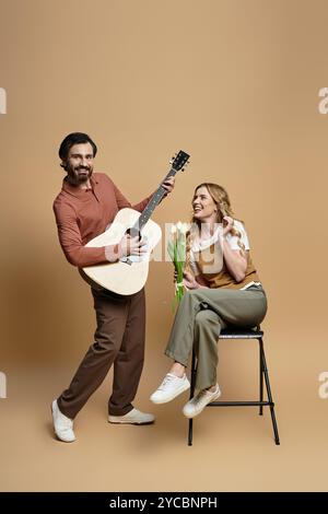 Ein fröhlicher Mann spielt Gitarre, während eine Frau mit frischen Blumen lächelt und Freude verbreitet. Stockfoto