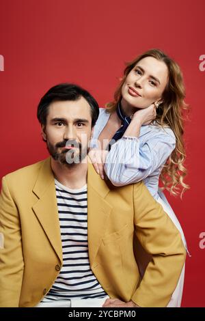 Ein bärtiger Mann in einer stilvollen Jacke sitzt selbstbewusst, während eine Frau spielerisch hinter ihm posiert. Stockfoto