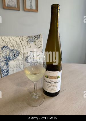Ein halbes Glas Weißwein steht neben einer Flasche Riesling auf einem Tisch mit Stuhl. USA Stockfoto