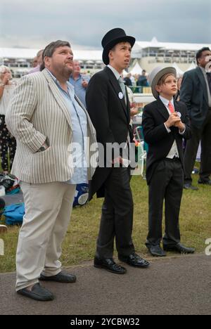 Arbeitergruppen, 2010er Jahre Großbritannien. Royal Ascot drei Freunde, zwei junge Männer in der Kleiderordnung des Tages, Oberhüte und formelle Schwanzmäntel und ein älterer Mann, der eher lässig gekleidet ist. Sie beobachten das Pferd, das auf einer riesigen Außenleinwand in der Heide läuft. Es sieht so aus, als würde es ihrem Pferd nicht so gut gehen. Ascot, Berkshire, England 18. Juni 2016 2010, UK HOMER SYKES Stockfoto