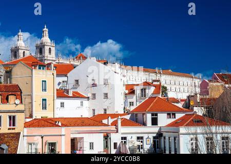 Entdecken Sie die atemberaubenden Dächer von Alfama mit den Doppeltürmen der Kirche Sao Miguel vor dem hellen Himmel von Lissabon. Stockfoto