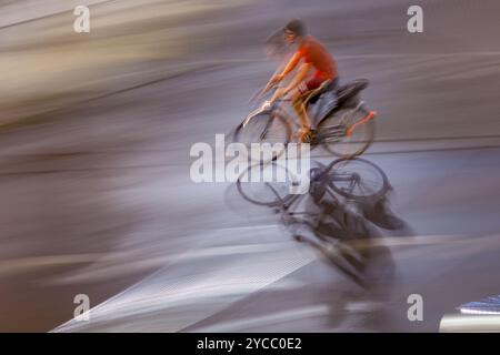 Dynamische Schwenkaufnahme, bei der ein Radfahrer bei Nacht schnell durch die Straßen der Stadt fährt und die Bewegung und das urbane Leben veranschaulicht. Stockfoto