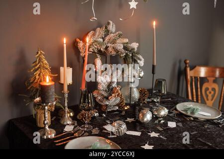 Festlicher Weihnachtstisch mit Kerzen und Geschirr im dunklen Stil, stilvolles Silvester-, Neujahrs- und Weihnachtsfest-Konzept Stockfoto