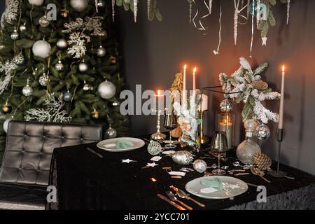 Weihnachten und Neujahr mit dunkler Innenausstattung des Zimmers. Festlicher Weihnachtsabend mit Kerzen auf dem Tisch und wunderschönem Geschirr Stockfoto