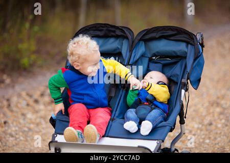 Junge und Kleinkind im Kinderwagen. Kind im Doppelwagen im Winter. Warme Kleidung für aktive Spaziergänge mit Ihrem Baby in der kalten Jahreszeit. Kleinkind im Kinderwagen. Stockfoto