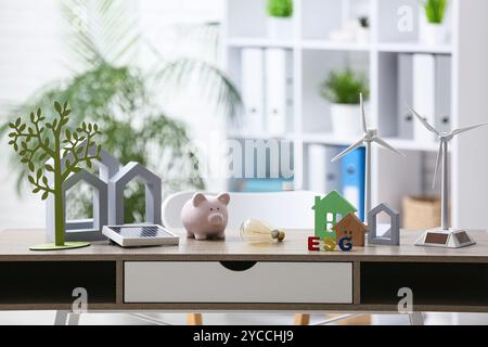 Windturbinenmodelle mit Schweinebank, Hausfiguren und Glühbirne auf dem Tisch im Büro. Konzept der grünen Energie Stockfoto