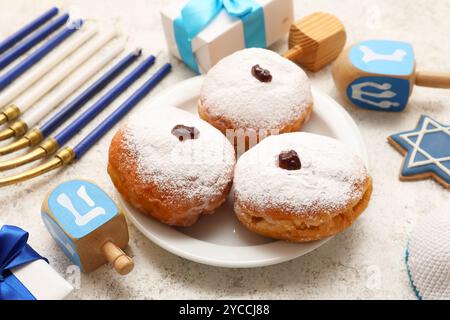 Komposition für die Hanukkah-Feier mit Donuts, Menora, Dreidels und Geschenkboxen auf weißem Grunge-Hintergrund, Nahaufnahme Stockfoto