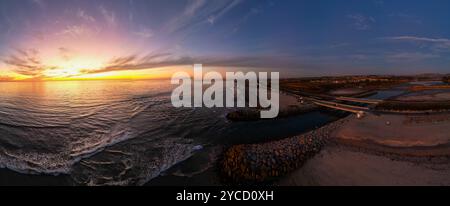 Ein Blick auf ein Carlsbad, Kalifornien, Sonnenuntergang mit dramatischen Farben in einem Panoramahimmel mit dem Carlsbad Batiquitos Lagoon Inlet Jetty bei Ebbe Stockfoto