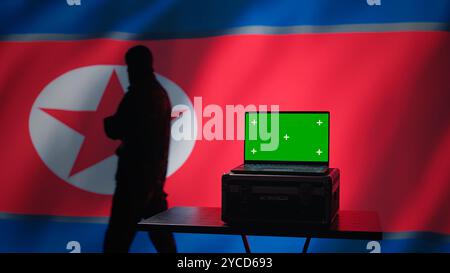 Der Geheimpolizistenagent Nordkoreas nutzt Massenpropaganda-Werkzeuge auf einem Green Screen-Laptop, um das Bewusstsein der Bevölkerung zu beeinflussen. Das Pjöngjang-Regime begeht PsyOP-Sabotage mit einem Modellgerät, Kamera B Stockfoto