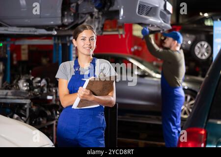 Die Autowerkstatt-Mitarbeiterin führt Aufzeichnungen über die Arbeit der Automechaniker in der Autowerkstatt – macht Notizen auf Papier Stockfoto