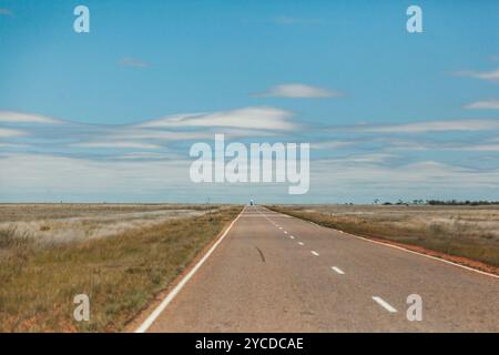 Eine lange, offene Straße zieht sich durch das karge Outback des Northern Territory und offenbart Australiens atemberaubende Wildnis unter einem hellblauen Himmel Stockfoto