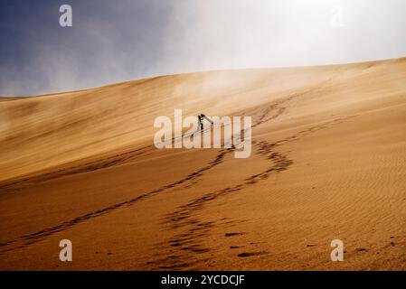 Ein einsamer Abenteurer, der eine riesige Düne im Valle de la Muerte, San Pedro de Atacama, hinunterfährt. Fußabdrücke folgen hinter dem Rücken. Stockfoto