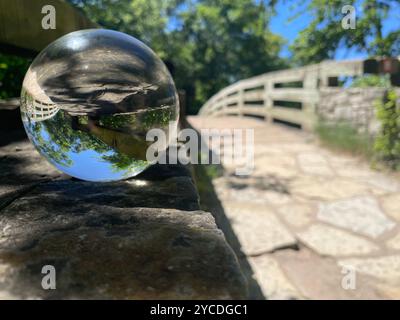 Kristallkugel auf einer Holzbrücke kehrt die Realität um. Bäume und Himmel spiegeln sich in perfekter Symmetrie und verschwimmen die Grenze zwischen Erde und Himmel. Stockfoto