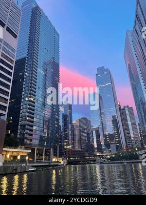 Chicago, IL, USA. Glashochhäuser am Flussufer Chicagos spiegeln den dramatischen Sonnenuntergang wider, während die Korallenhimmel die Leinwand der Stadt schmückt. Stockfoto