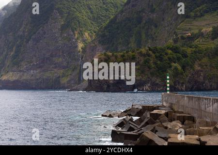 Küste mit großen Klippen von Seixal und Hafen mit dem Veu da Noiva Wasserfall im Hintergrund. Insel Madeira, Portugal Stockfoto