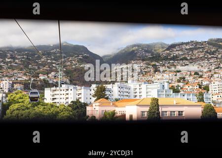 Seilbahn mit Hütten über der Stadtlandschaft von Funchal und Monte mit den Bergen im Hintergrund. Insel Madeira, Portugal Stockfoto