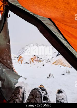 Bergsteigen im Winter: Blick nach außen aus einem orangen Zelt: Eine kalte Winterberglandschaft, ein schneebedeckter Campingplatz. Andenszene i Stockfoto