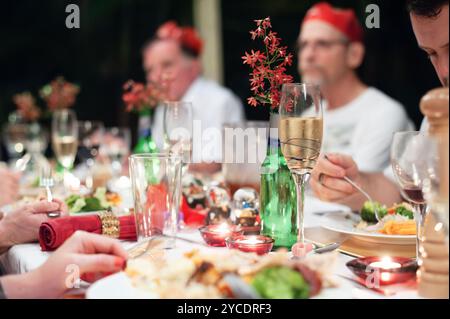 Eine Familie sitzt an dem in Rot und Grün und Gold dekorierten Esstisch und teilt ein Festmahl Stockfoto