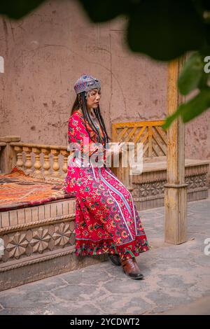 Kashgar, Xinjiang, China - 17. JULI 2023: Ein chinesisches Mädchen in traditioneller uigurischer Kleidung sitzt auf dem Holzsofa in der Straße von Kashgar Ancie Stockfoto