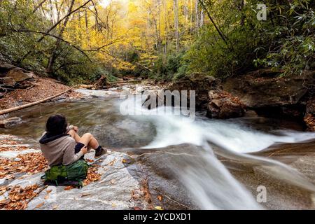 Wanderer sitzen in der Nähe der fließenden Kaskade am Looking Glass Creek im Herbst – Pisgah National Forest, nahe Brevard, North Carolina, USA Stockfoto