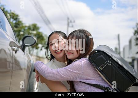 Eine fürsorgliche asiatische Mutter umarmt ihre entzückende kleine Tochter vor dem Schultor, nachdem sie sie am Morgen abgesetzt hat. Zurück zur Schule, happ Stockfoto