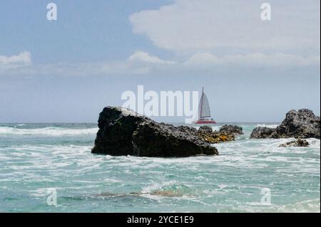 Ein Boot, das auf der Insel Reunion vor den felsigen Ufern des Grand Fond Beach an der Westküste der Insel durch den Indischen Ozean segelt Stockfoto