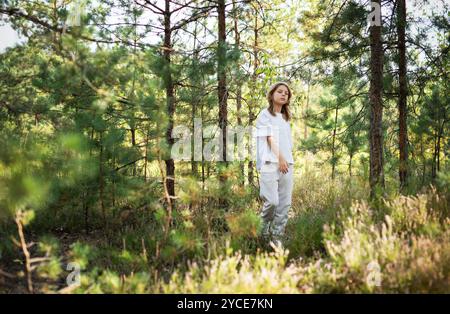 Ein kleines Kind spaziert ruhig auf einem Waldweg und genießt die Wärme der Sonne und die Ruhe der umliegenden Bäume und Pflanzen Stockfoto