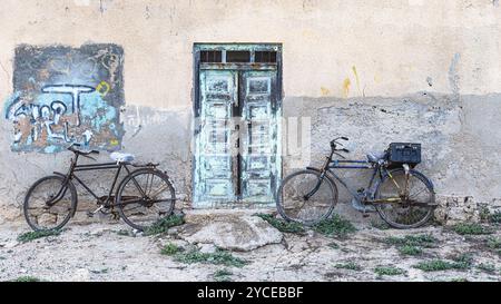 Alte Fahrräder, die mit einer alten Holztür gegen eine Hauswand gelehnt sind, am Strand von Salalah, Provinz Dhofar, Arabische Halbinsel, Sultanat Oman Stockfoto