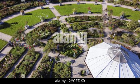 Beeindruckender Blickwinkel auf den Rosengarten des Botanischen Gartens Planten un Blomen. Leute (Gruppe von Papstkindern), die auf grünem Gras sitzen: Entspannen, essen vielleicht d Stockfoto