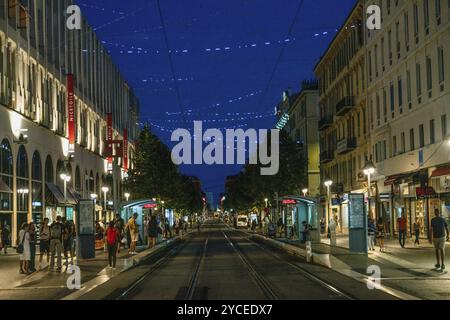 09-01-2022Nizza FR Av, Jean Medecin in der dämmerung, Menschen, die an Straßenbahnhaltestellen laufen und warten, Straßenlaternen ogf Stadt beleuchtet in Nizza (Französische Riviera Stockfoto