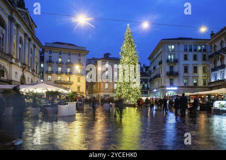 Fantastischer Blick auf den Weihnachtsbaum in Lugano am Reformationsplatz, unscharfe Bewegung, die Cafés für Menschen (draußen), die in blauer Stunde geöffnet wurden! Leute posieren für Phoro an Stockfoto