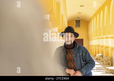 Porträt eines stilvollen, hübschen jungen Mannes mit einem Schal im Freien. Ein ernster Mann mit Hut und Jäckchen, der selbstbewusst in die Kamera blickt Stockfoto