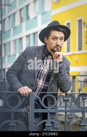 Porträt eines hübschen jungen Mannes mit einem Mantel im Freien. Ein ernster Mann mit Mantel, Hut und Hemd, der selbstbewusst in die Kamera blickt Stockfoto